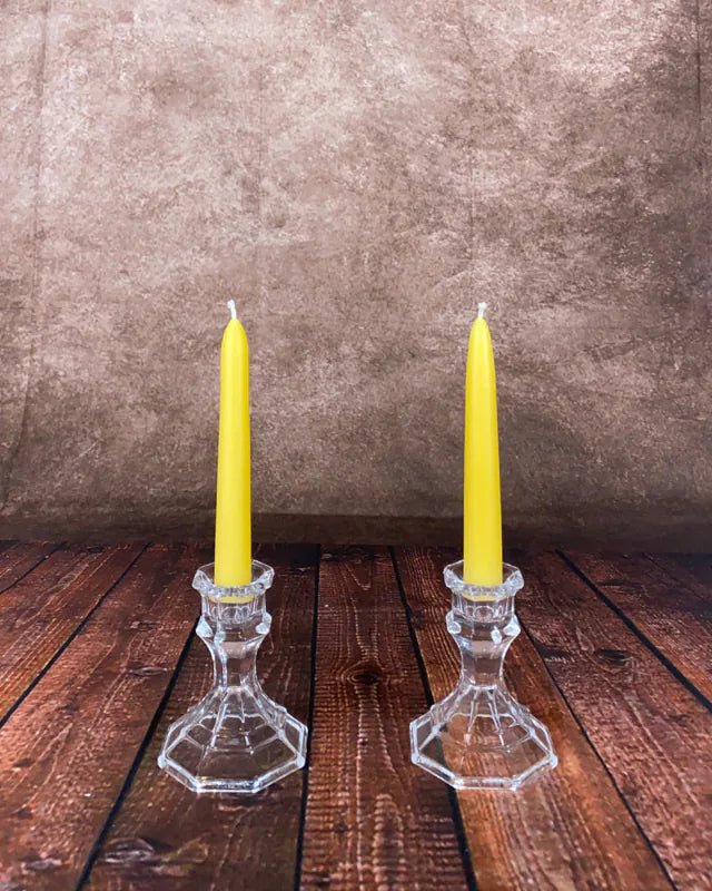 Two yellow candles in glass candlesticks on a wooden surface with a brown background